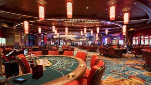 A casino with multiple blackjack tables, slot machines, and a large chandelier.