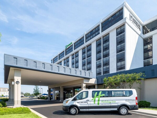 Un hotel moderno con vestíbulo cubierto y una furgoneta estacionada frente a él.