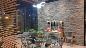 Un área de comedor moderna con una mesa de vidrio, sillas de madera y un fondo de pared de piedra.