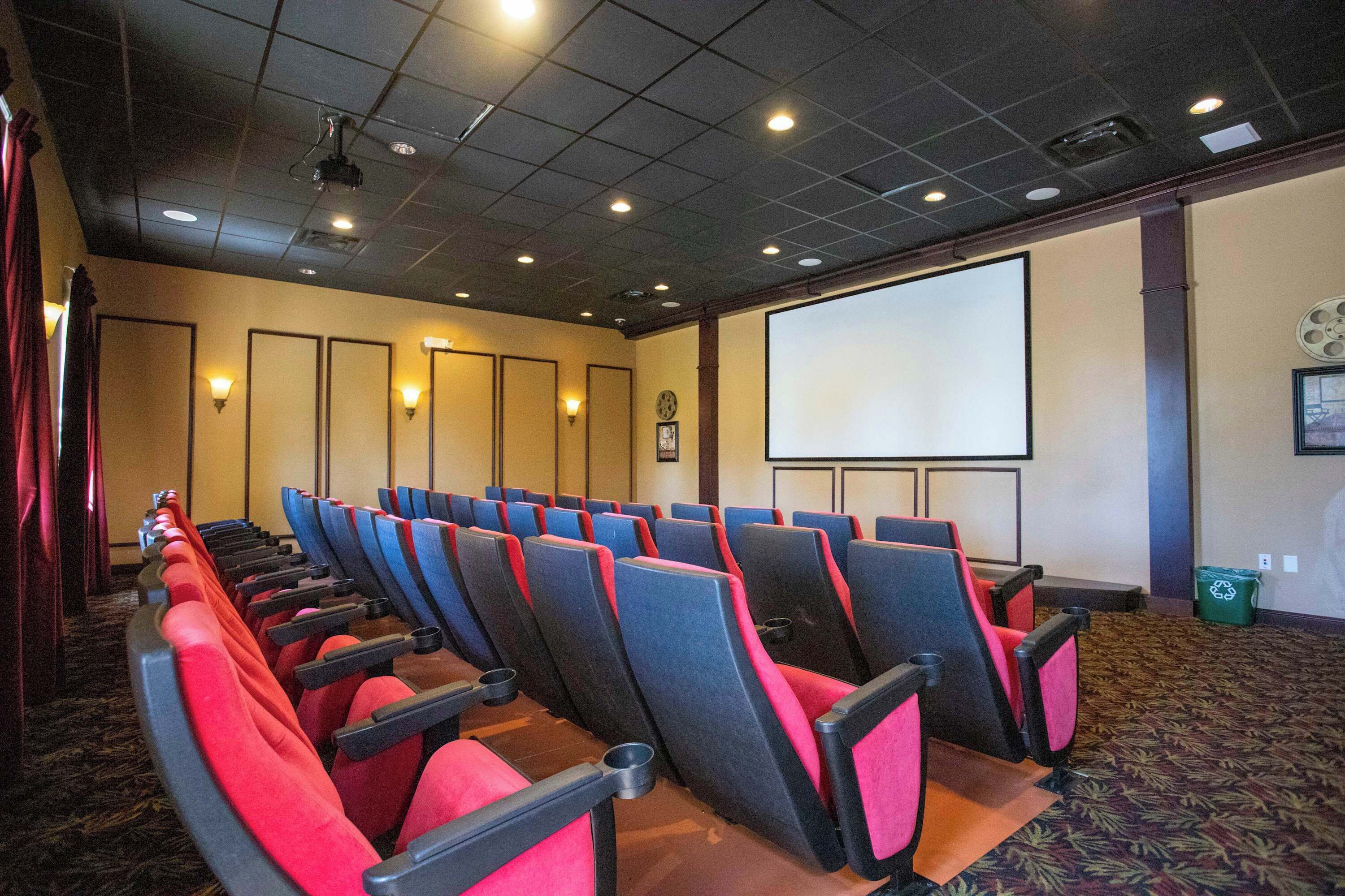 Ein Theater mit Reihen aus roten und schwarzen Sitzen, einer großen Leinwand und einem Teppichboden.