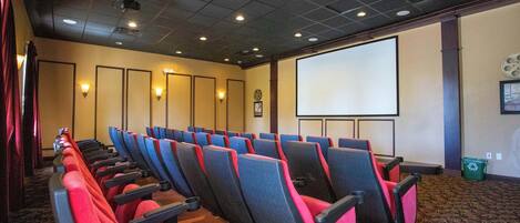 A theater with rows of red and black seats, a large screen, and a carpeted floor.