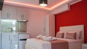 Ein modernes Hotelzimmer mit Küchenzeile, einem Bett mit Kissen und einer roten Akzentwand.