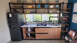 Une cuisine compacte équipée d’une cuisinière à gaz intégrée, d’un réfrigérateur et de divers ustensiles de cuisine rangés sur des étagères.