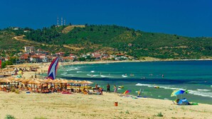 Ein Strand mit Sonnenschirmen, Menschen und einer Stadt im Hintergrund.