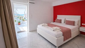 Ein modernes Hotelzimmer mit einem großen Bett, einer roten Akzentwand und Blick auf einen Balkon mit Außenmöbeln.