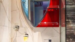 Ein Badezimmer mit einem herzförmigen Spiegel, einem weißen Waschbecken und einem roten Handtuchhalter.