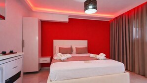 A hotel room with a red accent wall, a white bed, and a desk with a minibar. - House Blerina - Beachfront Double Sarti Getaway (Sithonia)