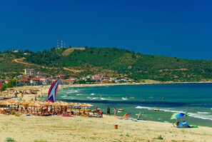 A beach with umbrellas, people, and a view of a town in the background. - House Blerina - Beachfront Double Sarti Getaway (Sithonia)