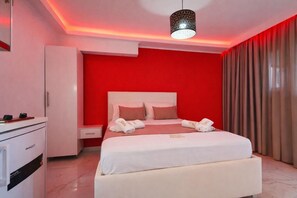 Una habitación de hotel con una pared de acento roja, una cama blanca y un escritorio con minibar.