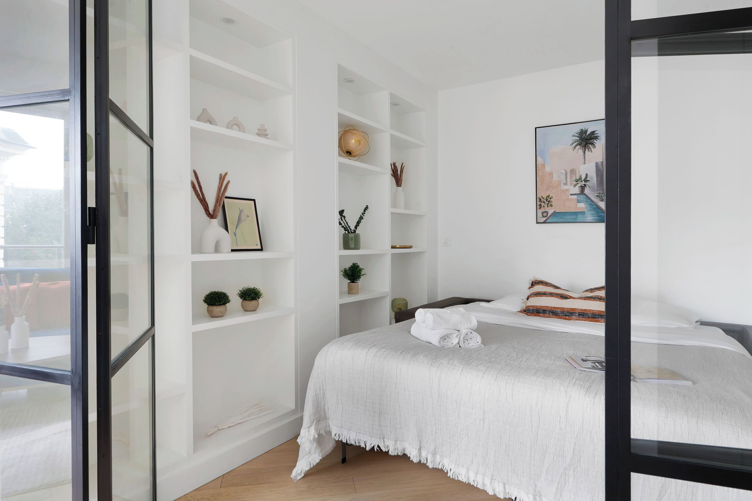 Een slaapkamer met een groot bed, witte schapenkasten en een schilderij aan de muur.