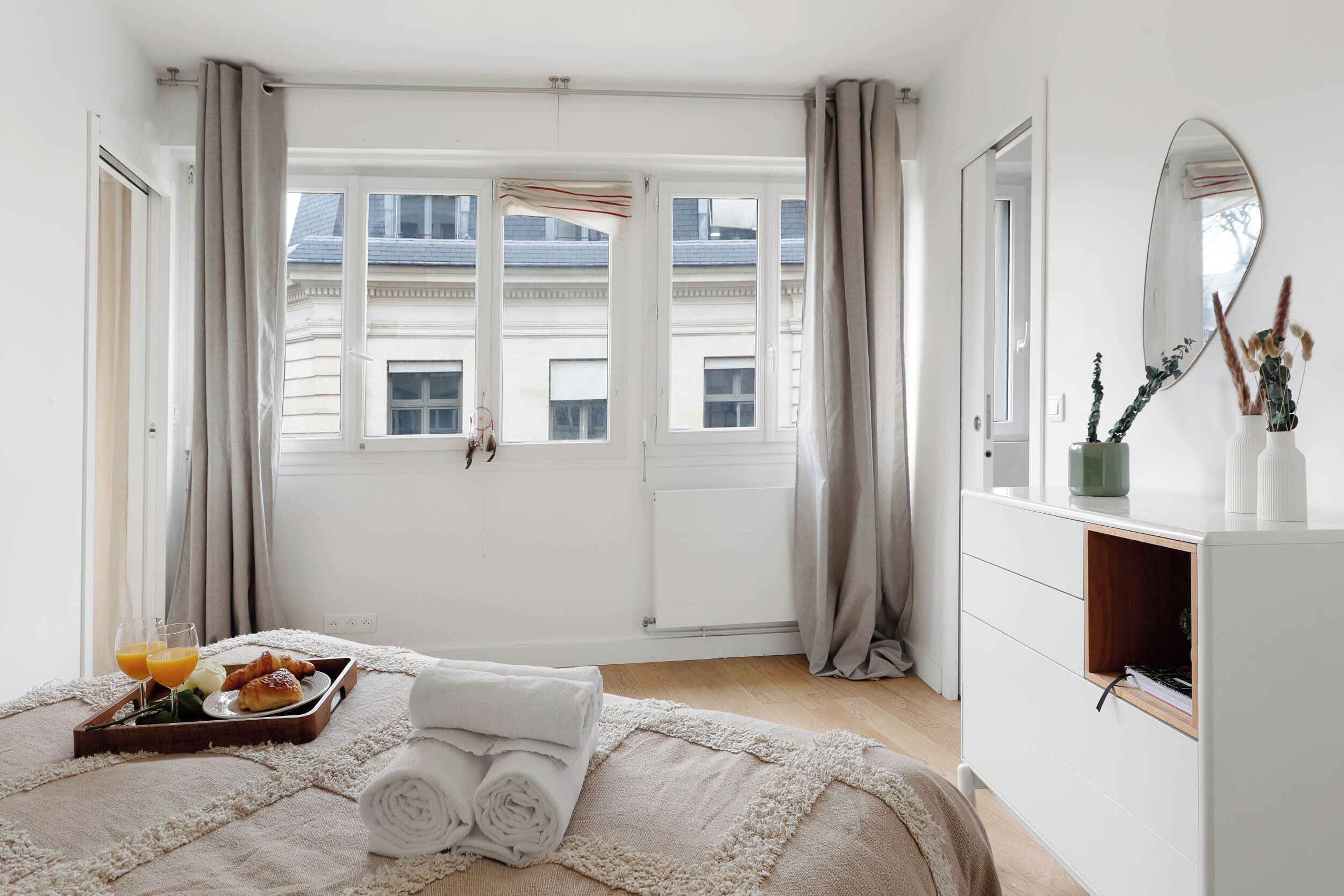 Ein Hotelzimmer mit Bett, Frühstücksbrett, Spiegel und einem Fenster mit Vorhängen.