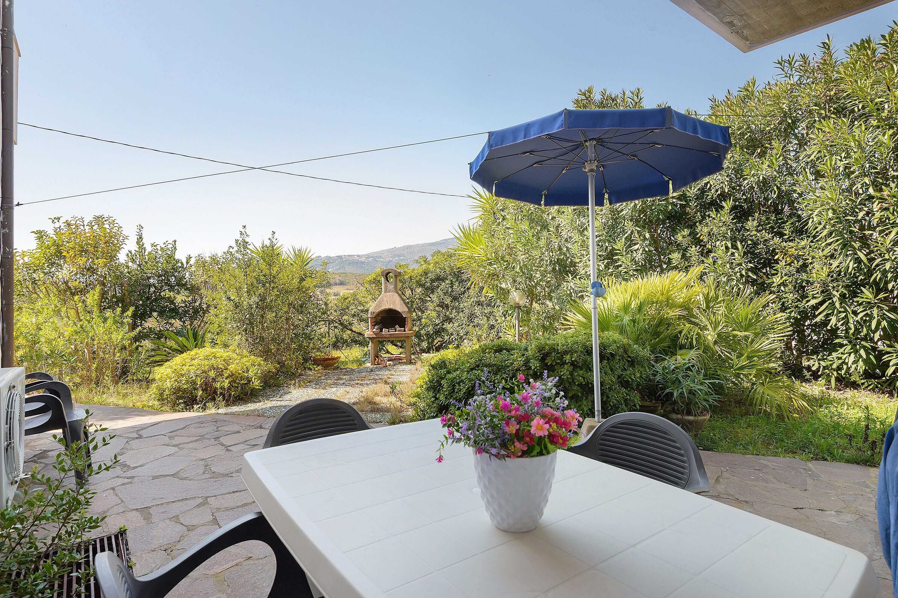 Une terrasse extérieure avec une table, des chaises, un parasol bleu et un vase à fleurs.