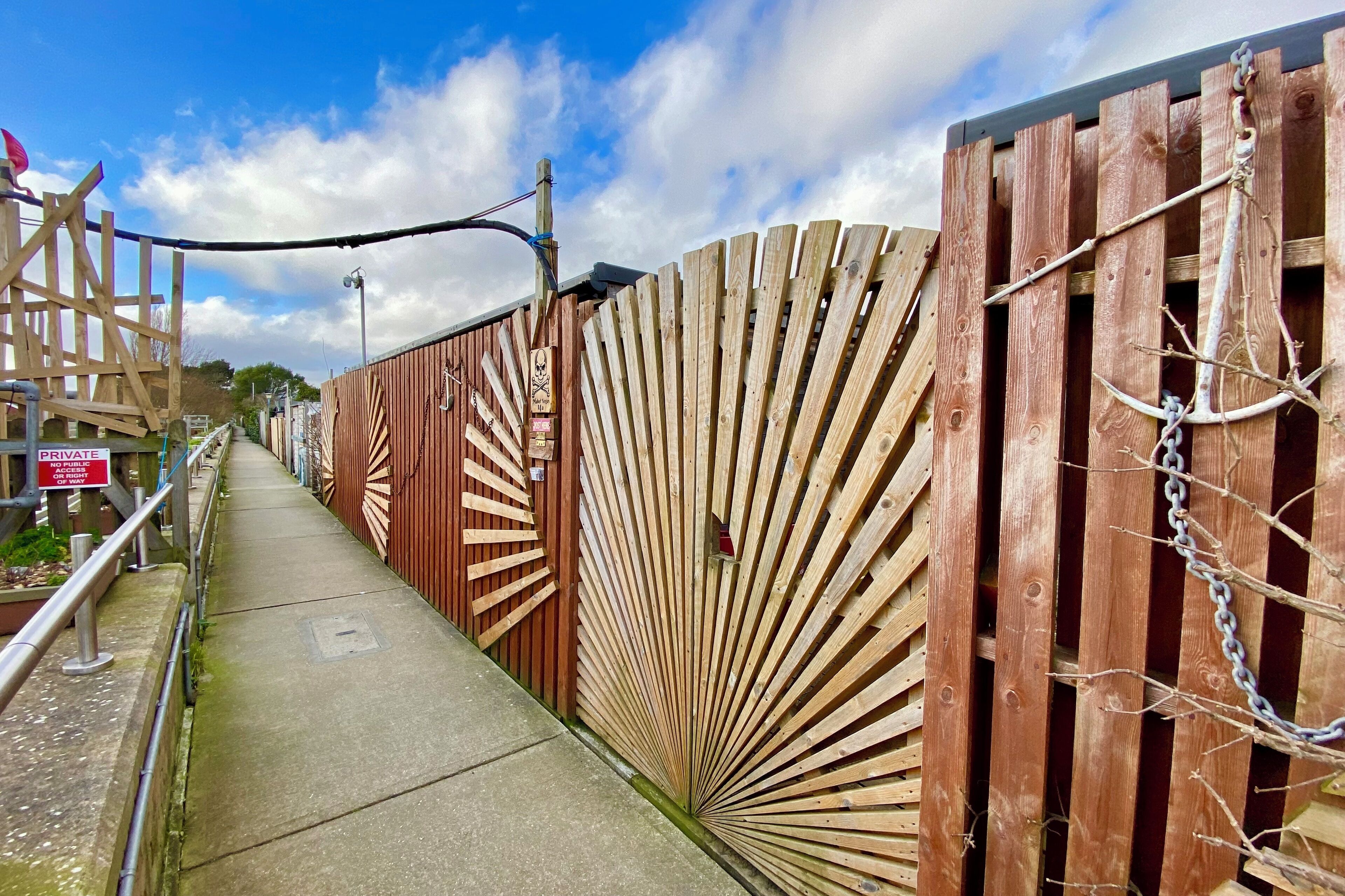 A wooden fence with a radial design, a metal gate, and a concrete pathway.