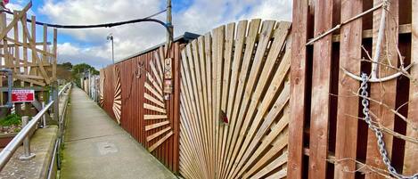 A wooden fence with a radial design, a metal gate, and a concrete pathway.