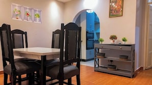Una zona de comedor con mesa y sillas, una consola gris con cestas, y una estantería en la pared con objetos decorativos.