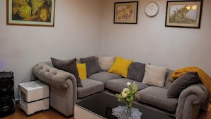 A living room with a grey sectional sofa, a small white side table, a black coffee table, and a framed wildlife painting above the sofa. - Darwendale Madhuve Lodge for one (Darwendale)