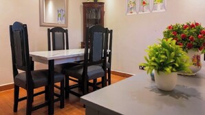 Un coin repas avec une table blanche et quatre chaises noires. Il y a un miroir au mur, un meuble avec des portes en verre et trois tableaux encadrés représentant des fleurs.