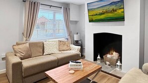 A modern living room with a sofa, a coffee table, a fireplace, and a painting on the wall. - Sleeps 8 3bedroom House, Harlaxton Garden Driveway (Harlaxton)