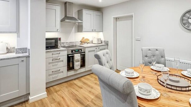 A modern kitchen with grey cabinets, a wooden dining table, and a grey upholstered chair. - Sleeps 8 3bedroom House, Harlaxton Garden Driveway (Harlaxton)