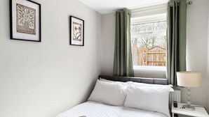 A neatly made bed with white linens, a bedside table with a lamp, and two framed artworks on the wall. - Sleeps 8 3bedroom House, Harlaxton Garden Driveway (Harlaxton)