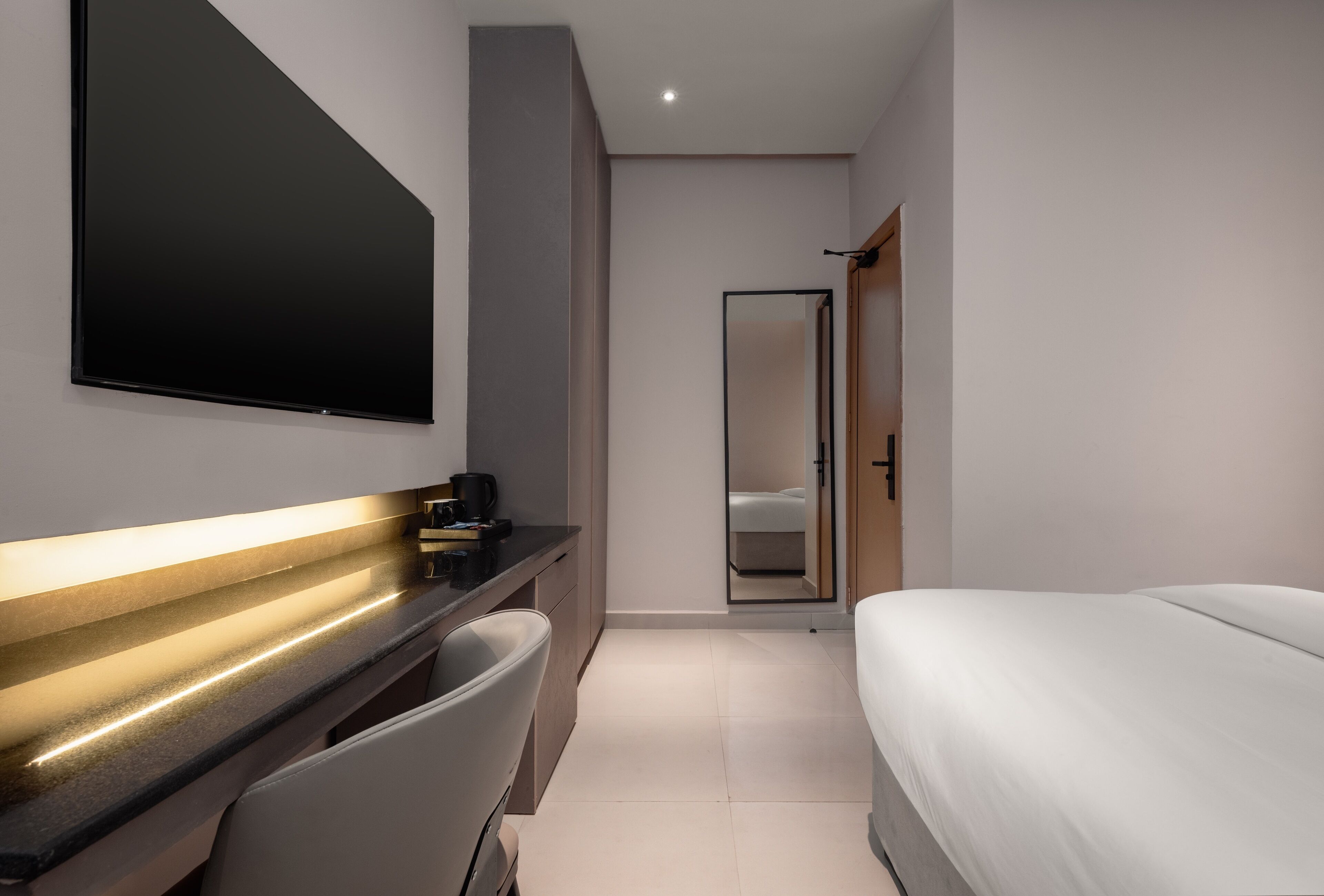 Et moderne hotelværelse med en stor seng, et fladskærms-tv monteret på væggen, et indbygget skrivebord med stol og et stort spejl.