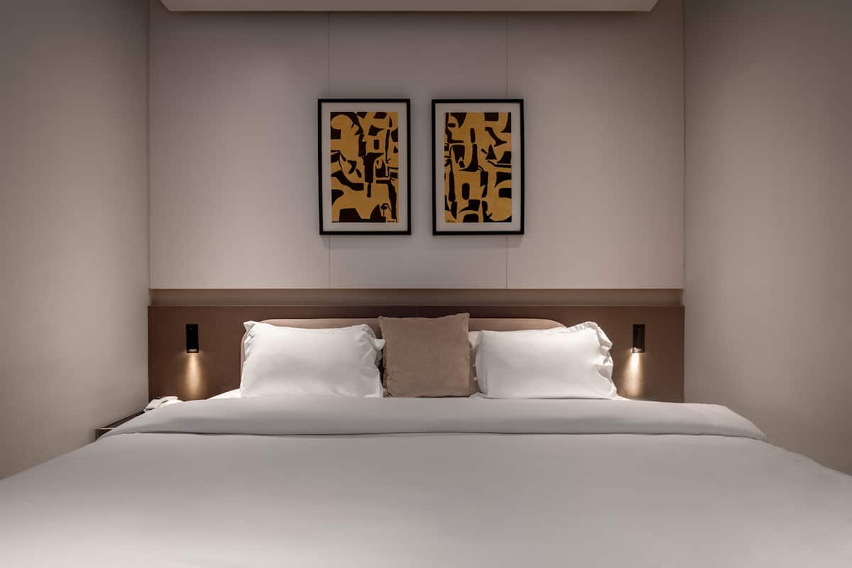 Une chambre moderne avec un grand lit, deux lampes fixées au mur et deux œuvres d’art abstraites encadrées.