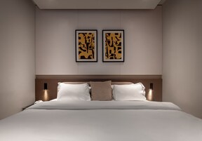 A modern bedroom with a large bed, two wall-mounted lights, and two framed abstract artworks.