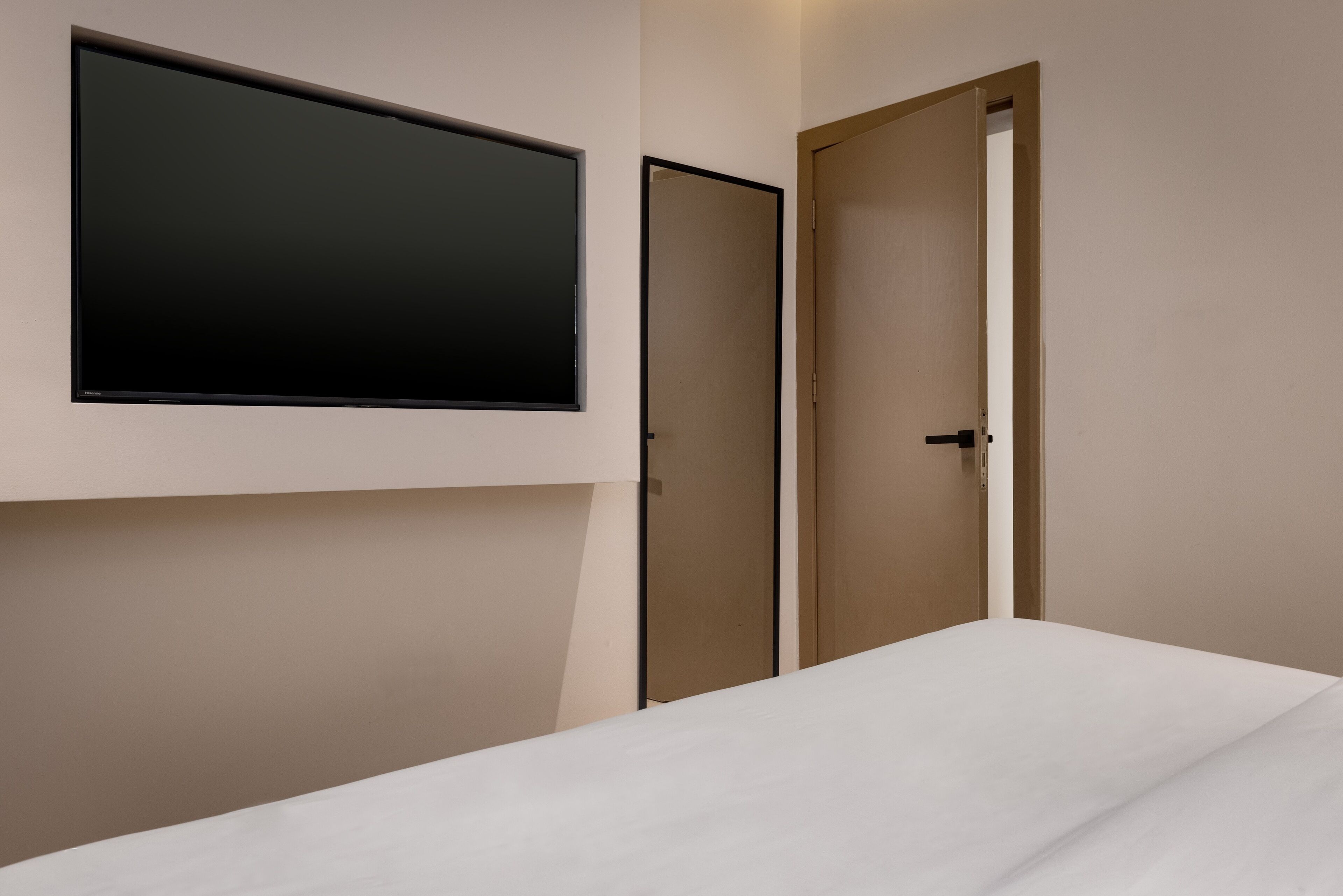 A room with a bed, a mounted TV, and two closed doors.