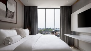Een moderne hotelkamer met een groot bed, een flatscreen televisie en een stadszicht door de vloerhoogte ramen.