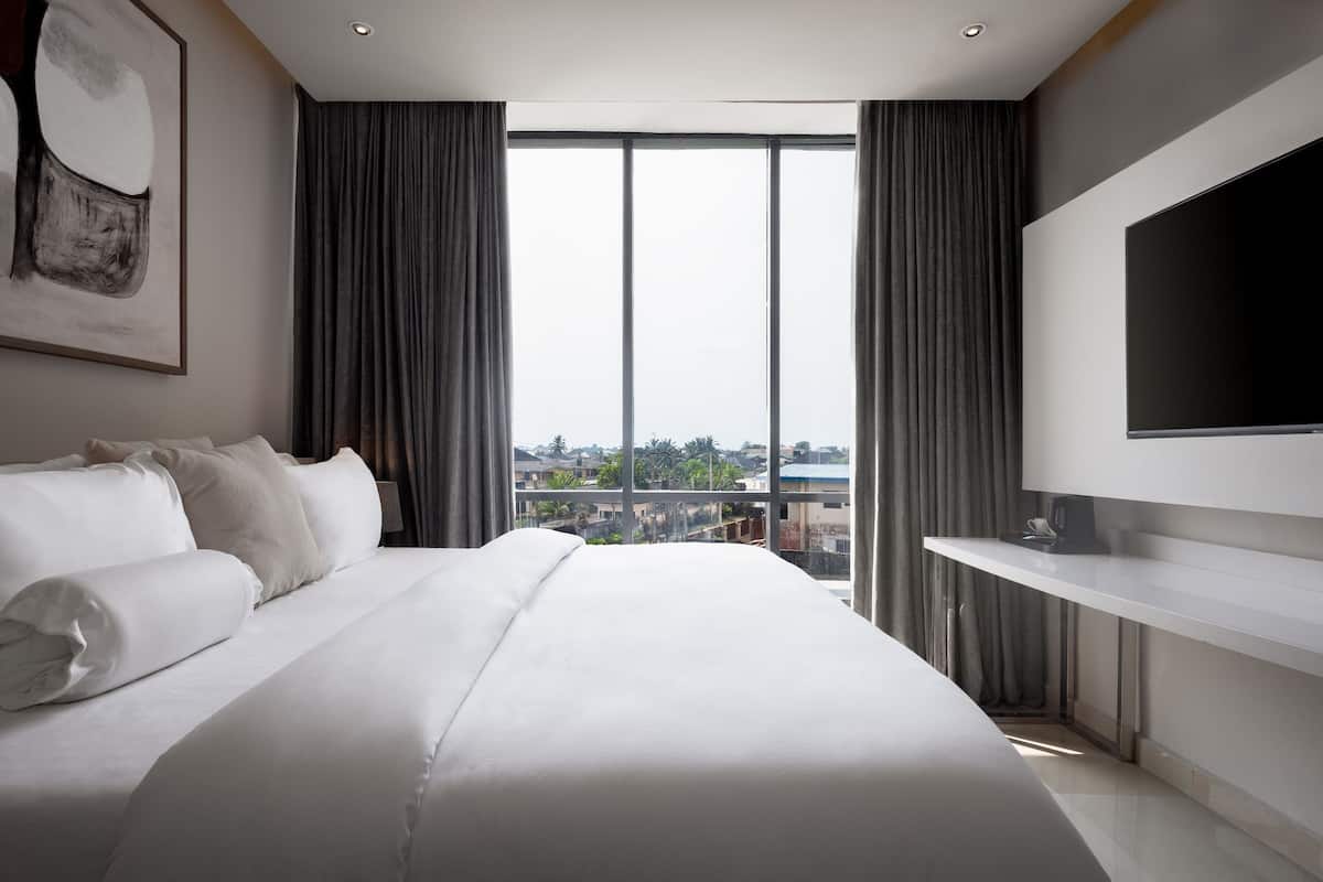 Une chambre d’hôtel moderne dotée d’un grand lit, d’un téléviseur à écran plat et offrant une vue sur la ville grâce à de grandes fenêtres du sol au plafond.