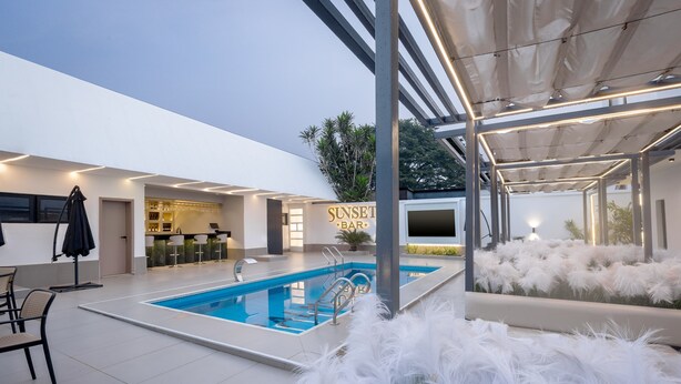 Een modern buitenzwembad met een bar, zitplaatsen en een bord waarop staat 'Sunset Bar'.
