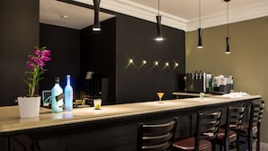 A bar area with a long counter, bar stools, pendant lighting, a potted plant, and a cocktail glass. - The World Hotel by Wecare Hosting (São Paulo)