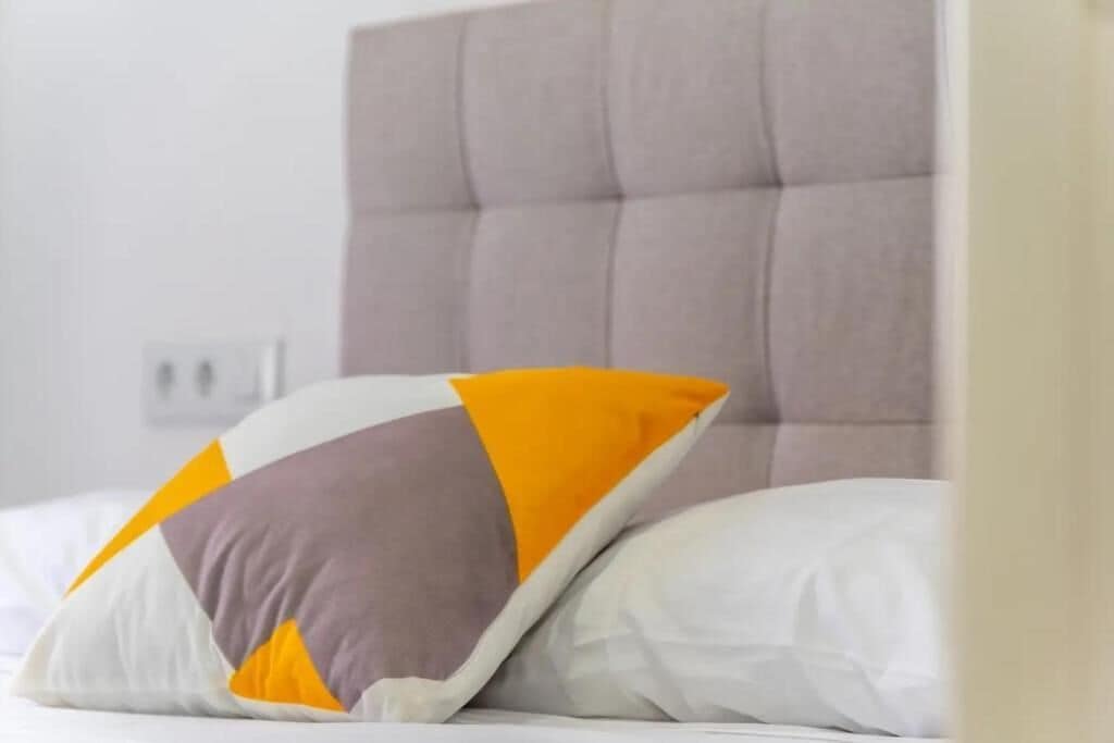 Ein Bett mit einem karottenartigen Kopfteil und Kissen in Weiß, Gelb und Grau.