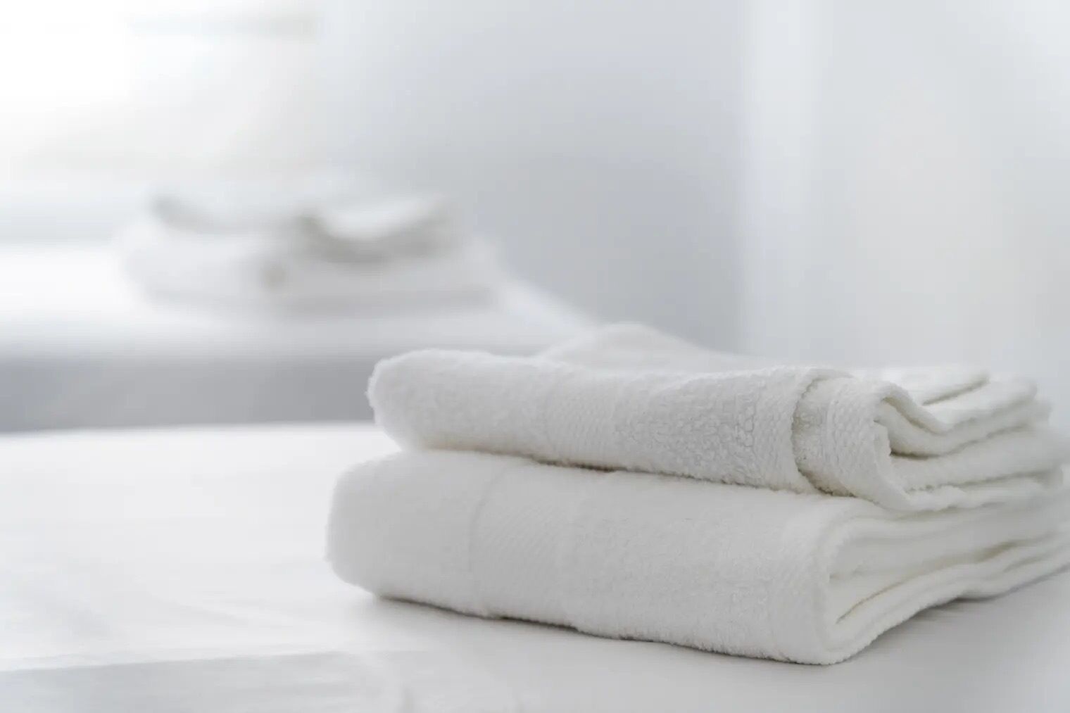 A stack of white towels on a white surface.
