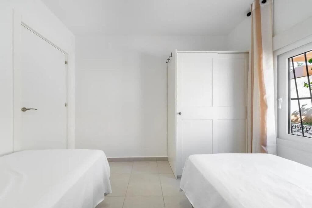 A room with two beds, white walls, a door, and a window with curtains.