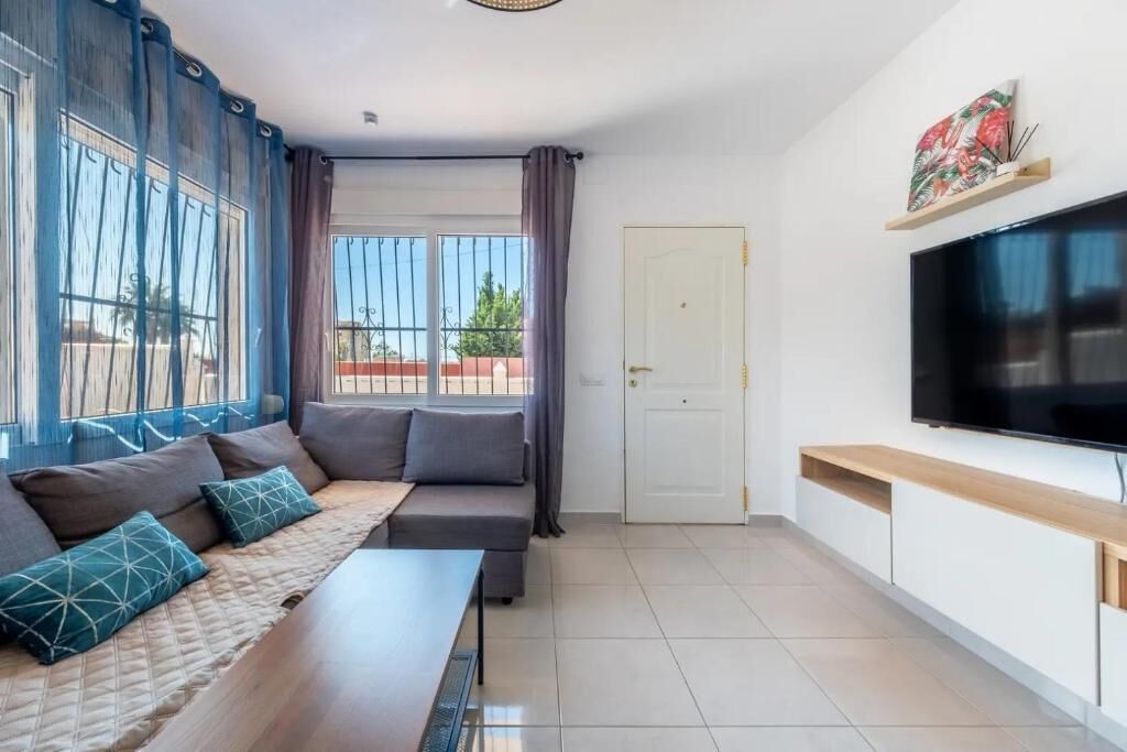 Een moderne woonkamer met een bank, een aan de muur bevestigde televisie en een raam met gordijnen.