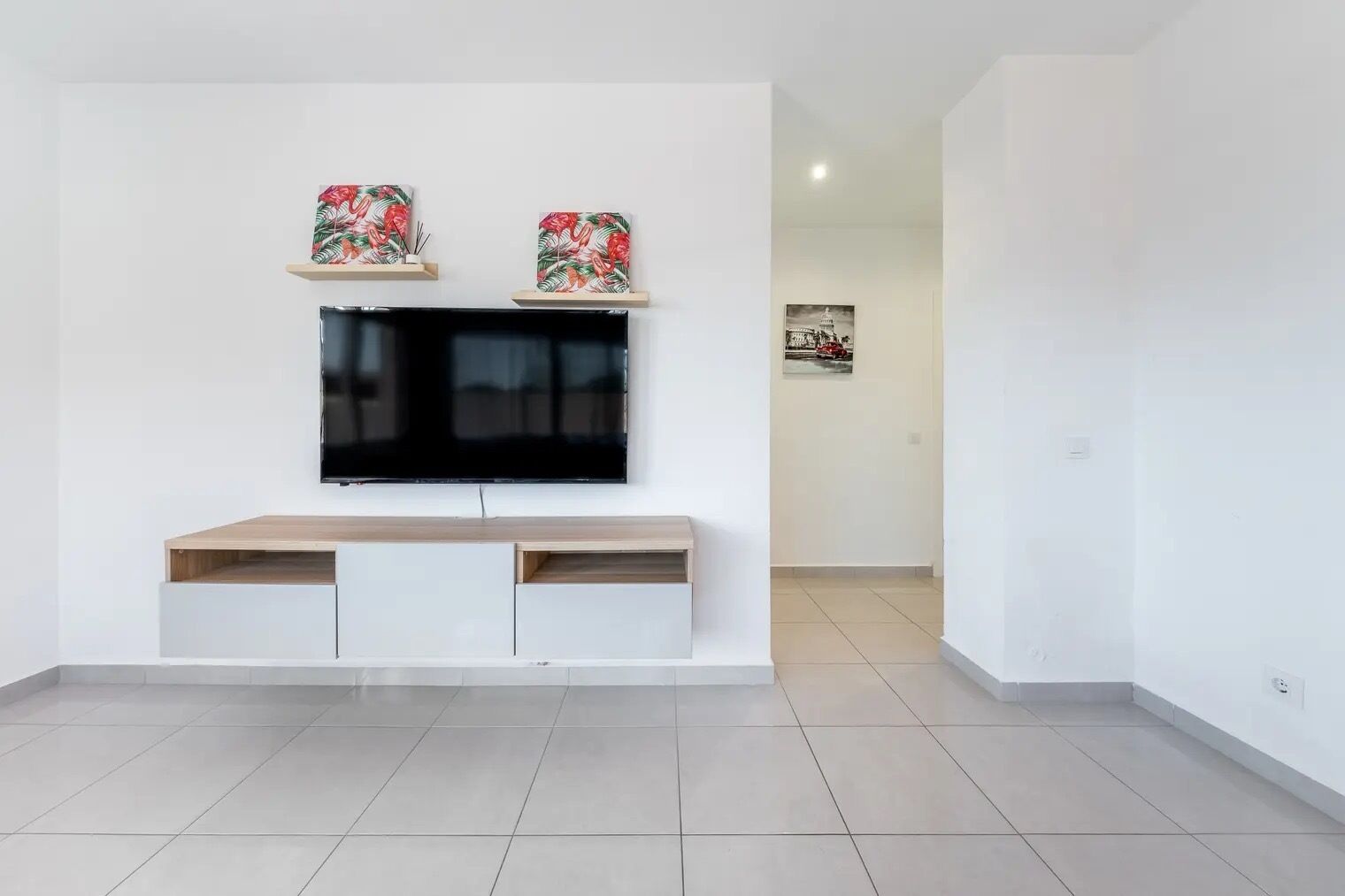 Ein modernes Wohnzimmer mit einem an der Wand montierten Flachbildfernseher, einem Holztische unterhalb sowie zwei dekorativen Wandbildern darüber.