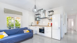 A modern kitchen with white cabinets, a built-in oven, and a refrigerator. There is a blue sofa with yellow pillows in the living area. - CASA LAS CALAS (Torrevieja)
