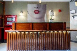 Un comptoir d’accueil avec un plateau en verre et des lattes en bois, un poste de commande pour les systèmes de lutte contre l’incendie, et une grande œuvre d’art fixée au mur.