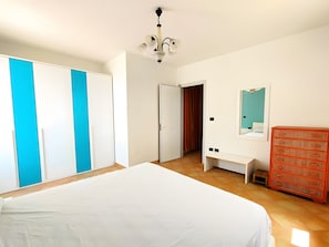 Un dormitorio con cama, armario, cómoda, espejo y una puerta que da a otra habitación.