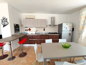 Une cuisine moderne équipée d’une cuisinière, d’un four, d’un évier et d’un réfrigérateur. On y trouve deux tabourets de bar et une table avec un saladier.