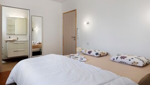 A bedroom with a bed, two pillows, a bedside table, a mirror, a wardrobe, and a door. - Guest Room Sous le Pin “Room 1” with Shared Terrace, Wi-Fi, and Air Conditioning! (Les Sables-d'Olonne)