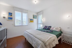 A bedroom with a bed, two windows, a TV, and artwork on the wall. - Guest Room Sous le Pin "Room 3" with Shared Terrace, Wi-Fi and Air Conditioning! (Les Sables-d'Olonne)