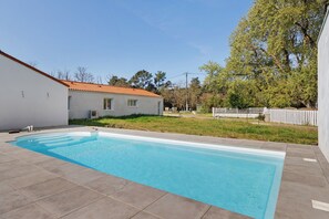 A rectangular swimming pool with a tiled deck, surrounded by a white building with a red roof, a white fence, and trees in the background. - Guest Room Sous le Pin "Room 4" with Shared Terrace, Wi-Fi, and Air Conditioning! (Les Sables-d'Olonne)