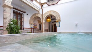 A swimming pool with clear water, surrounded by white walls and arches, with a fountain in the background. - Exclusive 5 Rooms Traditional House in Cordoba. Casa San Pedro (Córdoba)