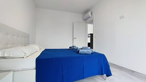 Ein Zimmer mit einem Bett, einem weißen Kopfteil, einer blauen Bettdecke und einer weißen Wand.