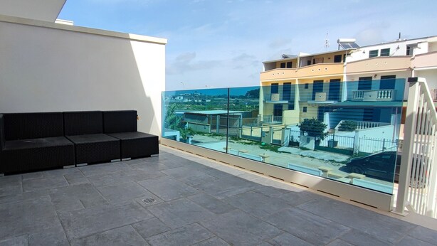 Ein Balkon mit einer schwarzen Couch, einer Glasreling und Blick auf Gebäude.