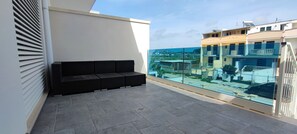 Ein Balkon mit einer schwarzen Couch, einer Glasreling und Blick auf Gebäude.