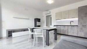 Eine moderne Küche mit Essbereich, weißen Stühlen, einer Marmorarbeitsplatte und grauen Schränken.
