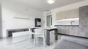 Una cucina moderna con zona pranzo, sedie bianche, un piano di lavoro in marmo e mobili grigi.